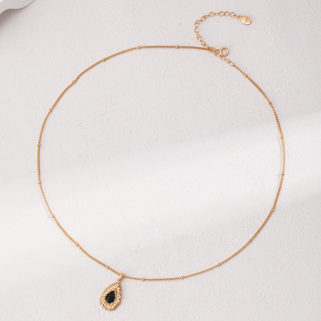Elegant gold chain necklace with a black teardrop pendant on a light textured background