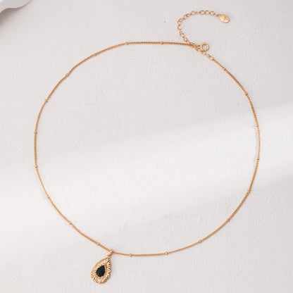Elegant gold chain necklace with a black teardrop pendant on a light textured background