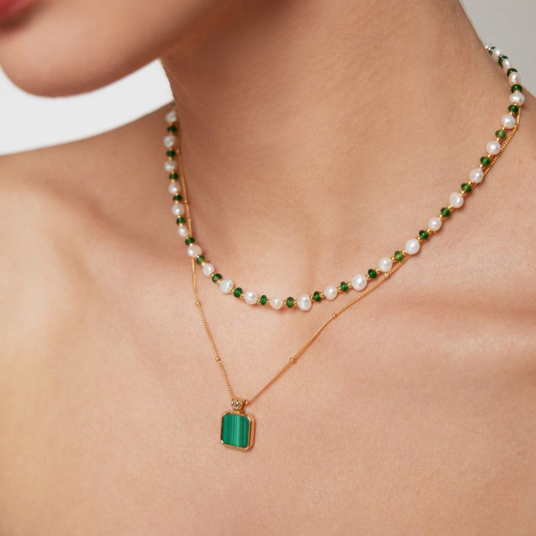 Close-up of layered necklaces with green beads, pearls, and gold chain with green pendant