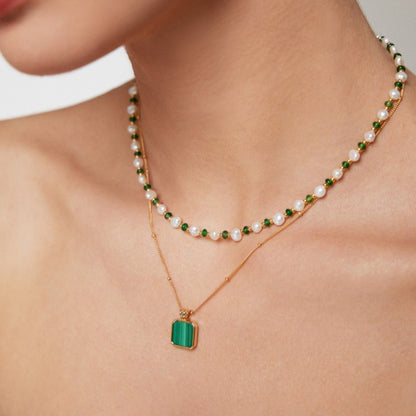 Close-up of layered necklaces with green beads, pearls, and gold chain with green pendant