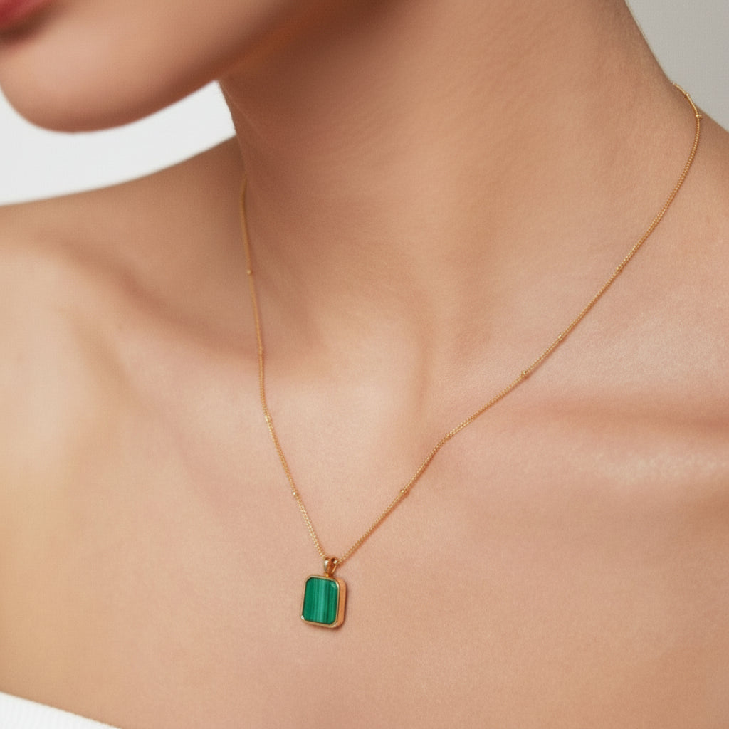Close-up of woman wearing gold necklace with green rectangular pendant on bare neck