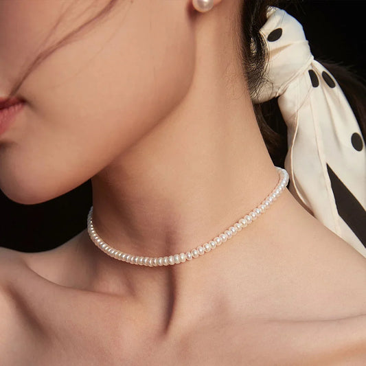 Close-up of woman wearing a delicate white pearl necklace and black polka dot hair scarf