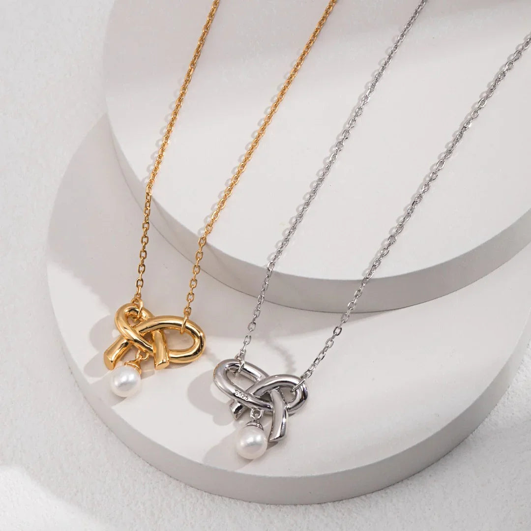 Gold and silver necklaces with knot pendants and single pearl charms displayed on white round stands