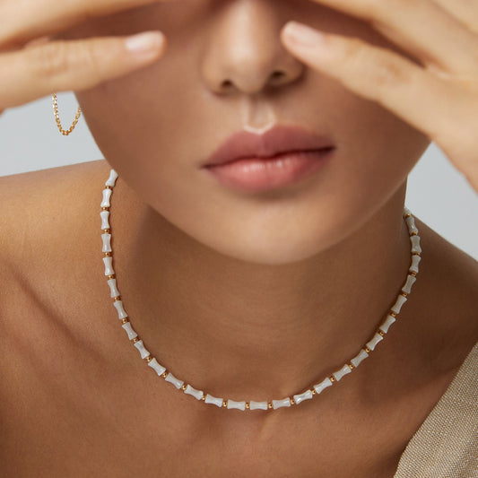 Close-up of a woman wearing a white and gold beaded necklace and a gold hoop earring by Chanqinfang jewelry