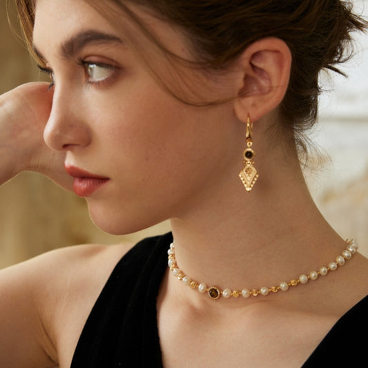 Woman wearing gold and black gemstone earrings with pearl and gold bead choker necklace