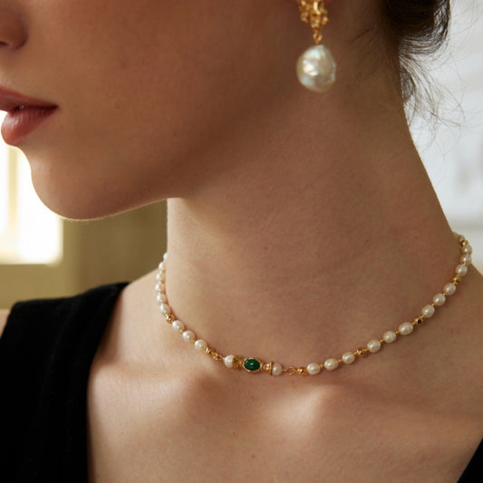 Close-up of woman wearing pearl choker necklace with green gemstone and gold accents plus matching pearl drop earring