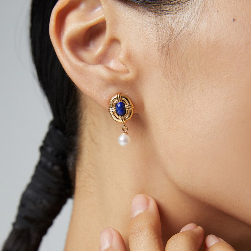 Close-up of gold earring with blue gemstone and dangling white pearl on woman’s ear