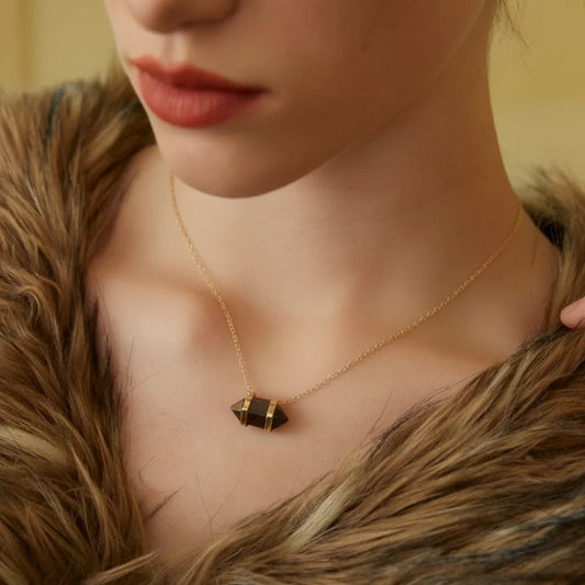 Close-up of woman wearing gold chain necklace with dark crystal pendant and brown fur collar