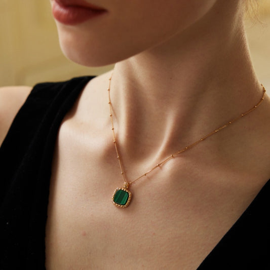 Close-up of woman wearing a gold chain necklace with a green gemstone pendant