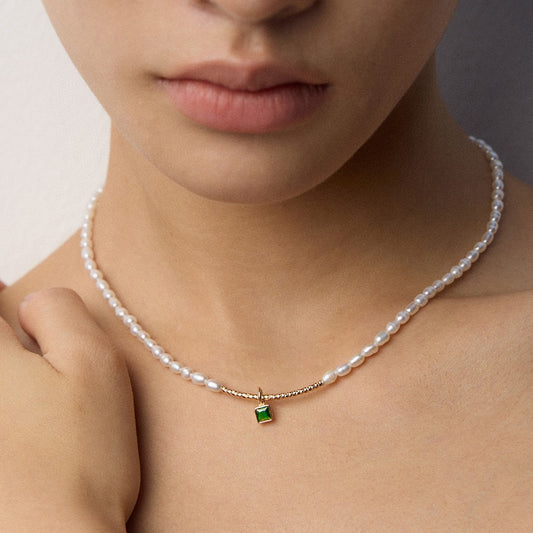 Close-up of a woman wearing a pearl necklace with a gold and green square pendant