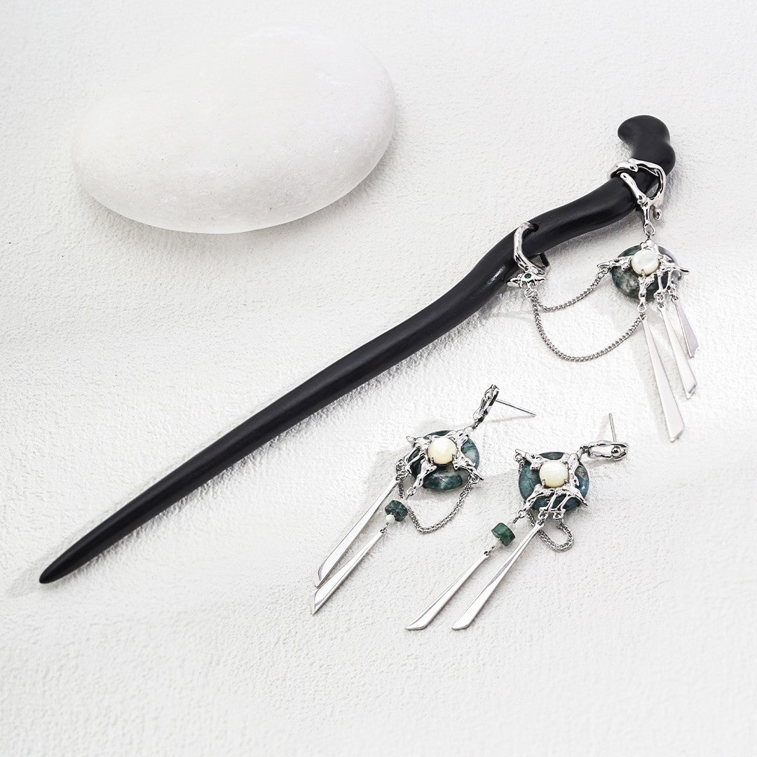 Black hair stick with silver and green stone decorative charms and matching silver dangling earrings on white textured background
