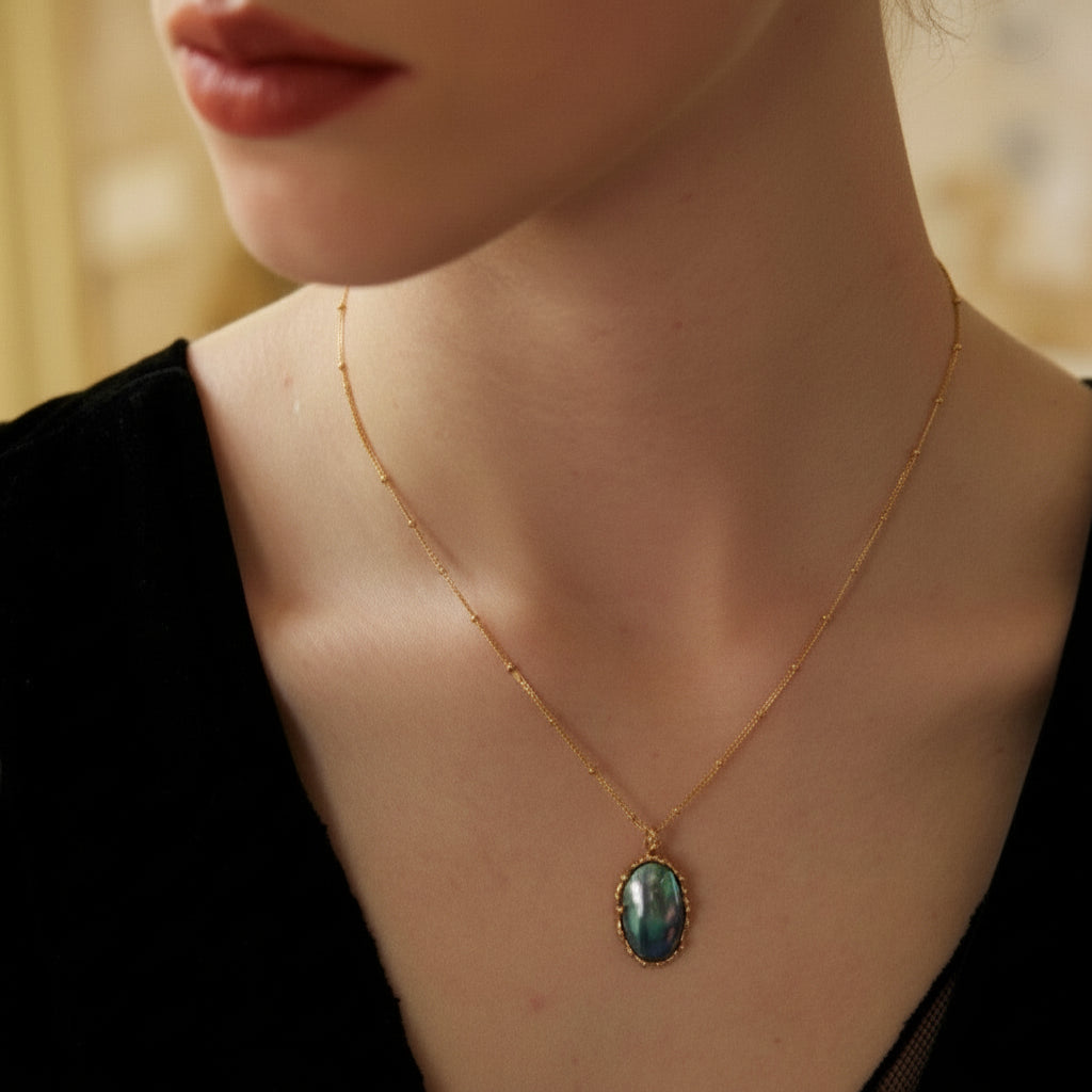 Close-up of woman wearing delicate gold chain necklace with oval iridescent stone pendant