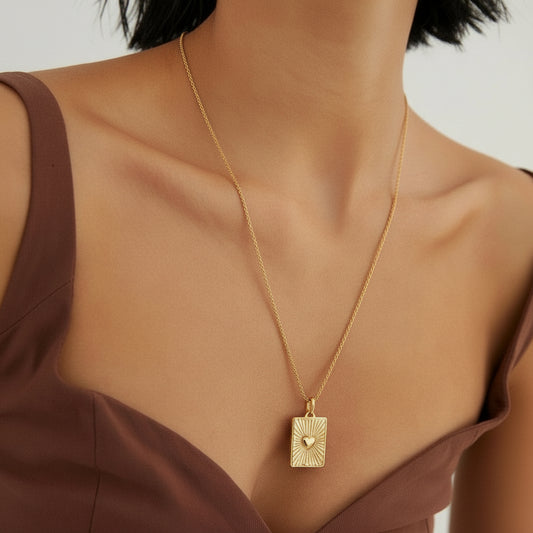 Close-up of gold rectangular pendant necklace with heart design on woman in brown top