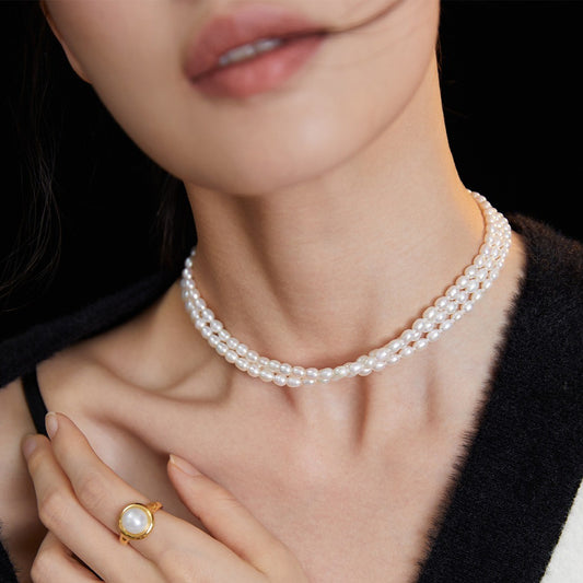 Close-up of woman wearing double-strand white pearl necklace and gold ring with large pearl