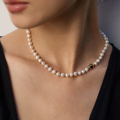 Close-up of woman wearing elegant pearl necklace with single black and gold bead on neck