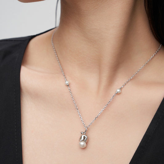 Close-up of a silver chain necklace with pearls and a unique silver pendant on woman's neck