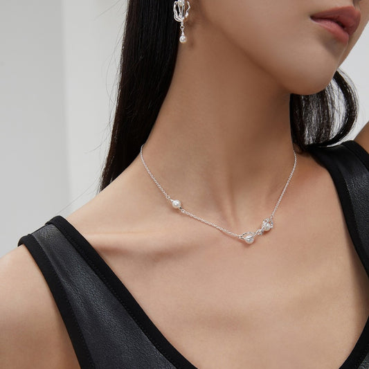 Close-up of woman wearing silver chain necklace and matching pearl drop earrings with black leather top
