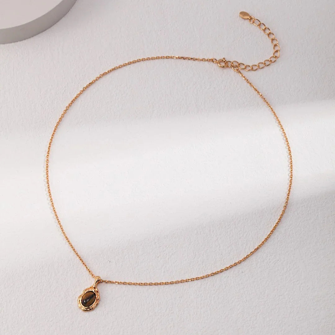 Delicate gold chain necklace with a small dark gemstone pendant on a light textured surface