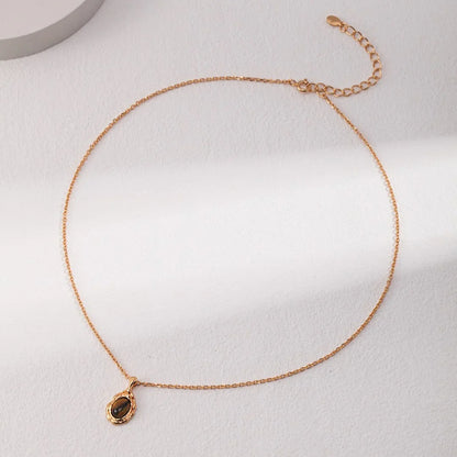 Delicate gold chain necklace with a small dark gemstone pendant on a light textured surface