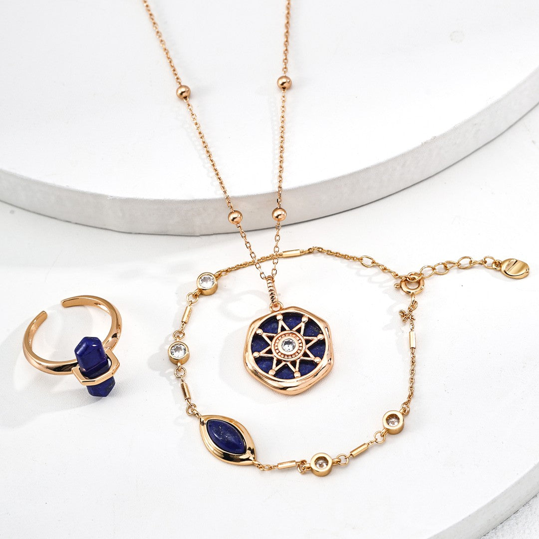 Gold ring with blue stone, gold bracelet with blue and clear stones, and gold necklace with circular blue pendant on white