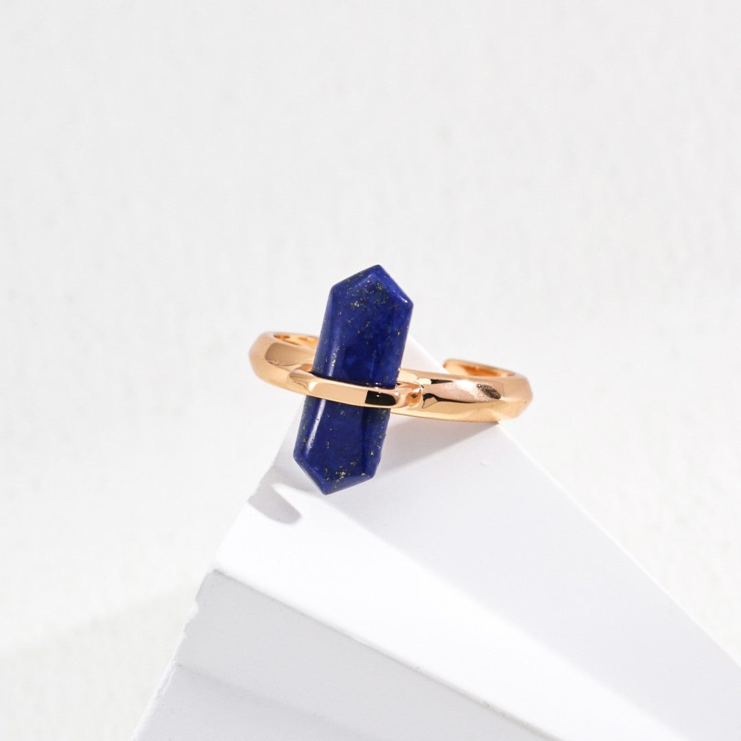 Gold ring with a polished blue gemstone resting on a white geometric surface